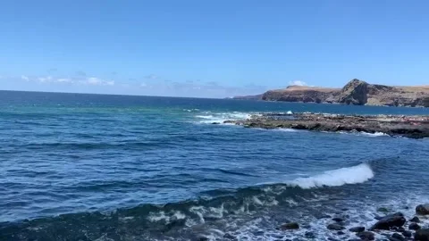 Serene Coastal Waves Dance Under the Brilliant Blue Sky and Rocky Cliffs Stock Footage 317095192
