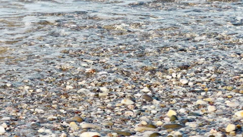 Serene Coastal Waves Gently Crash and Bubble Against a Smooth Pebble Beach Stock Footage 334122258