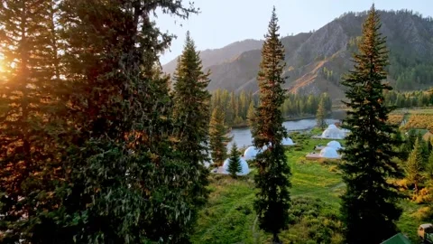 Serene Dawn By River. Rustic Domes At Dawn Amid Shimmering Waters And Sunlit Stock-Footage 338434709