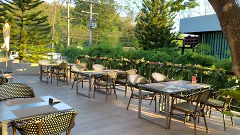 A serene empty outdoor cafe patio with tables and chairs surrounded by lush.. Stock Footage 333936104