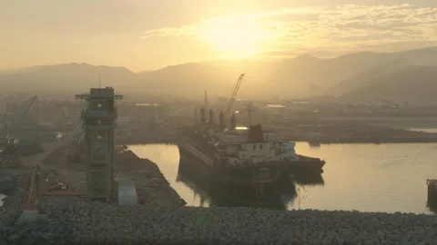 Serene harbor at sunset with a cargo ship docked and mountains in the background Stock Footage 324572863