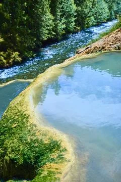 Serene Hot Spring Overlooking Flowing River in Forest - Eye-Level View Stock Photos