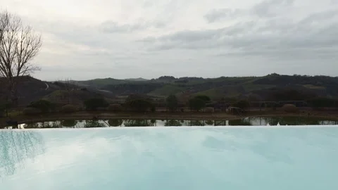 Serene infinity pool overlooking rolling countryside hills and reflective water Stock Footage 331977070