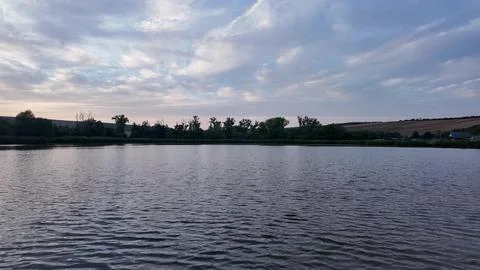 Serene lake landscape with dramatic clouds at sunset over rolling hills Fotos Stock