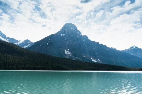 Serene lake view beneath imposing mountain peaks and cloudy sky. Stock Photos