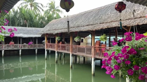 A serene landscape featuring a calm pond reflecting trees and a thatched-roof Stock Footage 317700101