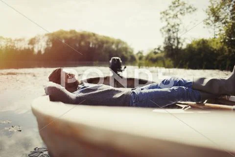 Serene man laying relaxing in canoe on sunny lake Stock Photos