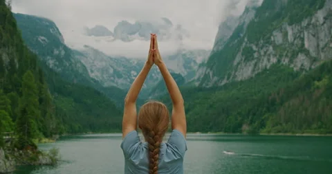 Serene mountain lake reflecting dramatic alpine peaks, with a woman practicing Stock Footage 306527557