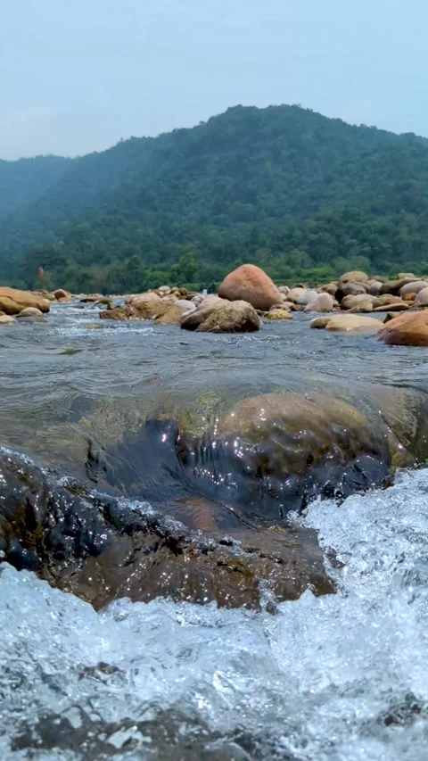 Serene mountain landscape with flowing river and rocky foreground under a c.. Stock-Footage 338414712