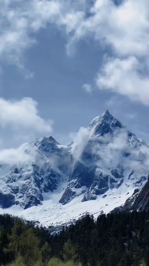 A serene mountain landscape with snow-capped peaks under a blue sky with clouds Vidéo 333021785