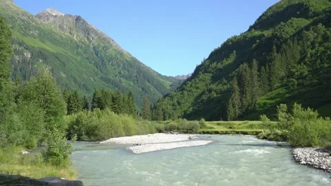 Serene mountain river flowing through lush green valley 스톡 동영상 312735033