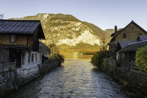 A serene mountain stream flows between rustic wooden houses Stock Photos