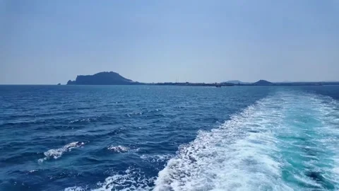 A serene ocean view with a boat wake and distant islands under a clear blue sky Vídeos de archivo 333022167