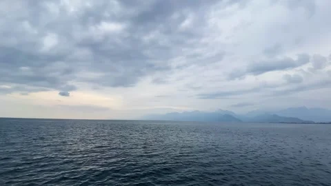 Serene Ocean View With Distant Mountains Under a Cloudy Sky at Dusk Stock Footage 264054226