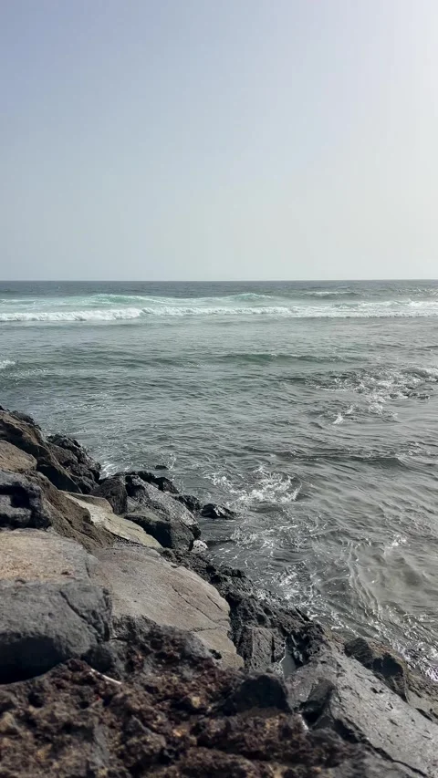 The Serene Ocean Waves Gently Crash Against the Rugged Rocky Shoreline, Creating Stock Footage 319008622