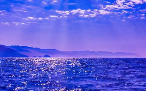 Serene Ocean Waves Reflecting Sunlight Amidst Misty Mountain Landscape Unde.. Stock Photos