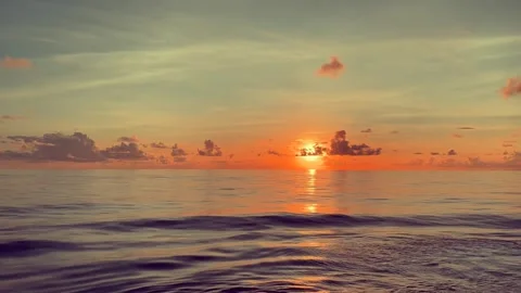 Serene ocean waves ripple beneath a vibrant sunset sky with scattered clouds Stock Footage 338281771