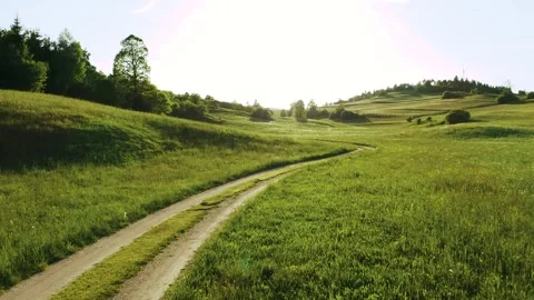 A serene path winds through a vast green meadow, bordered by rolling hills. Stock Footage 259074210