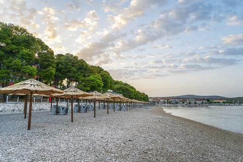 A serene pebble beach lined with rustic straw parasols under a blue sky Stock Photos