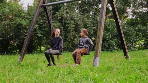 In a serene playground, a young mother interacts joyfully with a child on swings Stock Footage 316830089