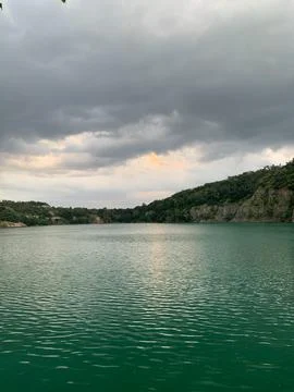 Serene quarry lake with dramatic clouds and lush green hillsides Stock Photos