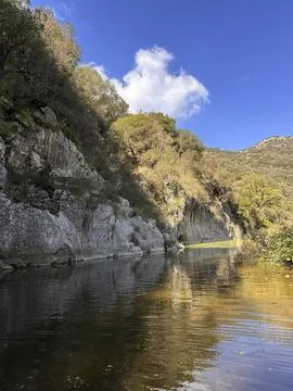 Serene river flowing between rocky cliffs under a clear blue sky with lush Stock Photos