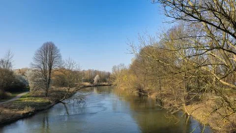 A serene river flows through a forest under a clear blue sky Stock Photos