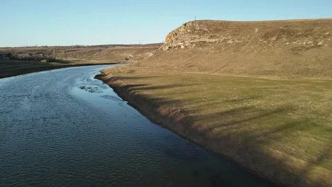 Serene river flows through grassy landscape with rocky hills under clear blue Stock Footage 332723600