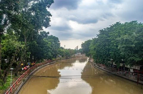A serene river flows through a lush, tree lined urban area under a cloudy s.. Stock Photos