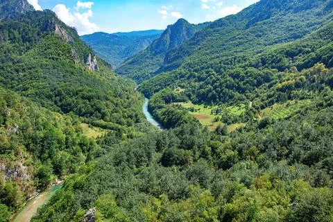 A serene river meanders through vibrant green valleys, framed by majestic mou Stock Photos