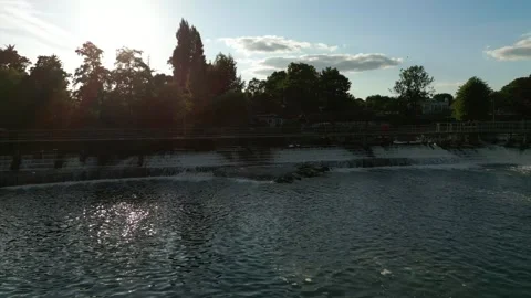 A serene river with a waterfall, bridge, and trees under a blue sky with cl.. Stock Footage 340545898