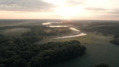 Serene river winds through the countryside as soft sunrise light illuminates Stock Footage 345084040