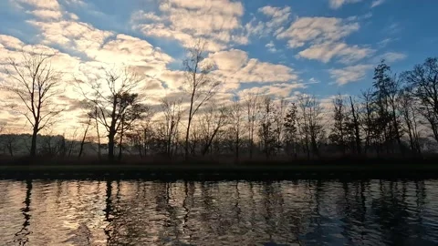 A serene riverbank sunset with reflected trees on calm water, creating beautiful Stock Footage 276362204