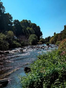 Serene rushing river flows through natural landscape with rocks and bridge .. Stock Photos