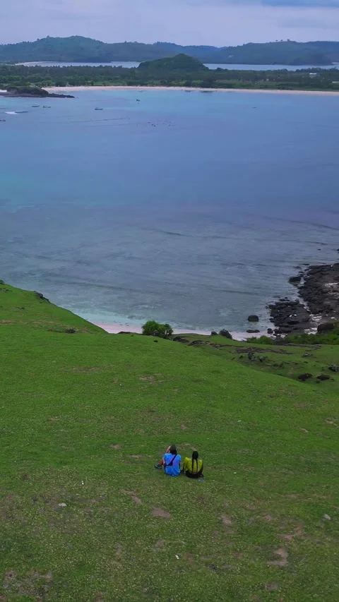 Serene scene of explorers resting on scenic cliffside overlooking bay Видео 335091139