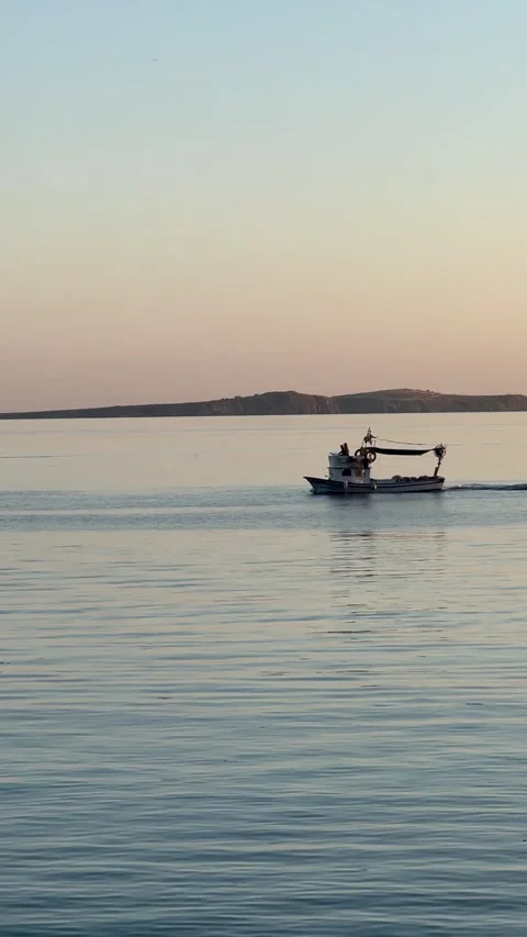 A serene scene of a small boat gliding across calm waters during sunset 動画素材 314070130