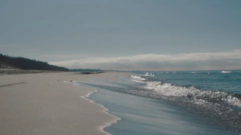 Serene sea waves gently rolling onto a tranquil, empty sandy beach on a sunny Vidéo 336702137