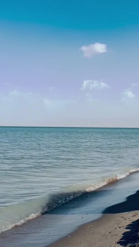 Serene seascape with gentle waves rolling onto a sandy beach under a clear blue Stockbeeldmateriaal 334163565