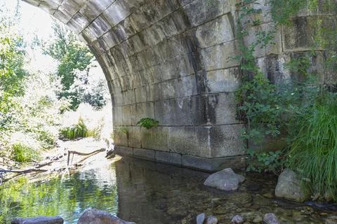 A serene stream flows beneath the Puente del Perdn, surrounded by lush gree.. Stock Photos