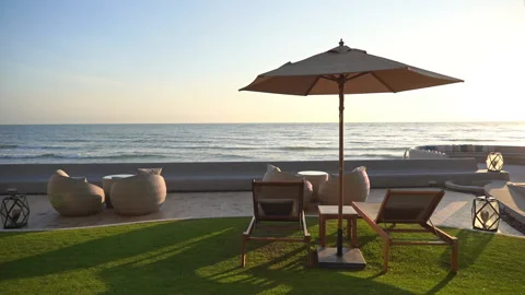 Serene sunset beach setting with lounge chairs and umbrella overlooking Vidéo 134440350