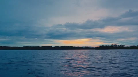 A serene sunset over a calm river with dense rainforest in the background in Stockbeeldmateriaal 345156392