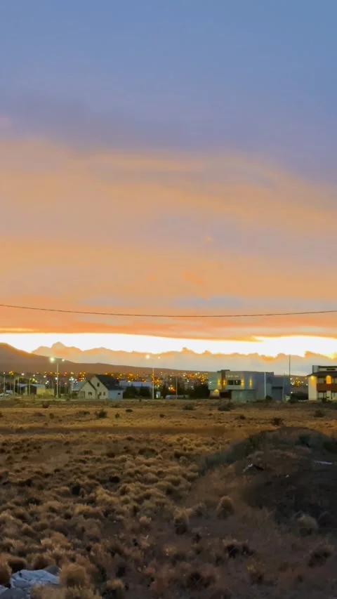 A serene sunset over a dry, grassy landscape with mountains and a small city in Stock Footage 276876451