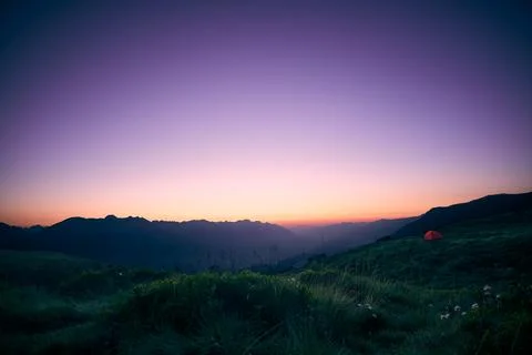 Serene sunset over mountain range with a lone tent nestled in lush grass Stock Photos