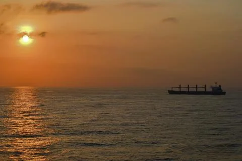 Serene Sunset Over Ocean with Cargo Ship Silhouette Stock Photos