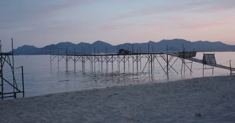 Serene sunset over a quiet beach with a wooden pier extending into calm waters Stockbeeldmateriaal 314077257