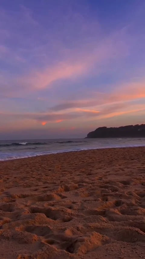 Serene sunset over a sandy beach with gentle waves rolling onto the shore under Vidéo 334164044