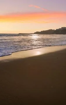 Serene Sunset Over Sandy Beach With Gentle Ocean Waves Reflecting Sunlight Stock Photos