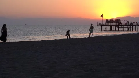A serene sunset view captures silhouettes of individuals by the beach, enjoying Stock Footage 317906494