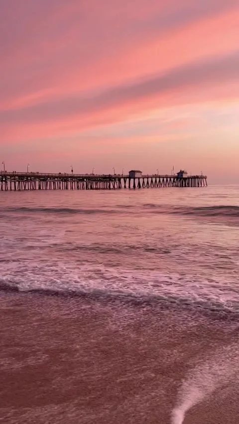 A serene video of a beach at sunset with a long pier stretching into the calm Vídeos de archivo 333022043