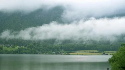 A serene view of an Austrian lake enveloped in fog, with misty mountains in the 스톡 동영상 281592463